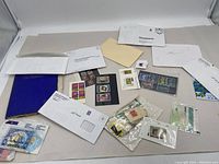 Wide view of assorted stamps, envelopes, and blue stamp album spread on a table, showing the overall variety in the lot.