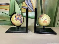 Pair of black metal L-shaped bookends each holding a small globe depicting world maps.