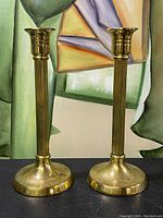 Front and side view of two tall brass candlesticks with rounded bases and fluted shafts.