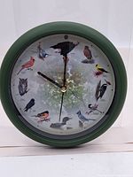 Full view of the clock showing entire face, green frame, and bird illustrations around the dial.