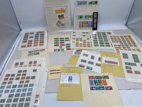 Wide view of multiple album pages and loose sheets containing numerous stamps of assorted countries and types, arranged on a white backdrop.
