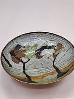 Top view of oval brass bowl showing enamel art with stylized trees and sun over water in earth tone colors.