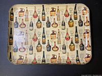 Top view of the vintage serving tray showing full pattern of liquor bottles and glasses on cream background with visible surface wear and cracks.