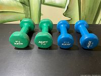 Four dumbbell weights by Alex in green and blue color placed on black surface.