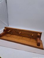 Full view of wood coat rack with shelf showing three wooden pegs and side supports.