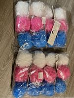 Eight loofah body scrubbers in packages with white, pink, and blue colors shown on a wooden floor.