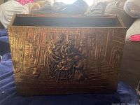 Full side view of brass magazine holder with relief art showing woman and children in indoor scene