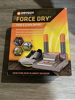 Front of the boxed DryGuy Force Dry Shoe & Glove Dryer showing branding, image of device, and key product features such as eliminating moisture and odor reduction.