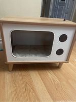 Wooden cat or small dog house with white front panel, large cutout entrance, circular side windows, and cushioned interior.