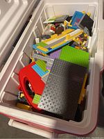 View inside white Coleman cooler showing multiple Lego baseplates in colors including green, gray, and white alongside many loose Lego bricks and pieces.