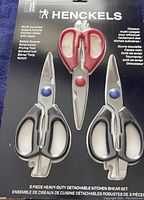 Front view of Henckels 3 piece kitchen shear set in original packaging showing red and black handled shears and multi-purpose tools.