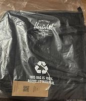 Herschel branded packaging indicating the bag is made from 100% recycled material with logo and recycle symbol.