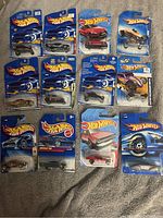 Lot of 12 Hot Wheels diecast cars in original sealed packaging, varying in model and color including blue, red, purple and gold.