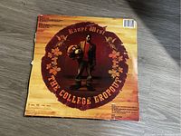 Back cover of the vinyl record showing Kanye West standing with teddy bear mascot and track listing in a circular floral design on a wooden background.