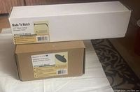 Two boxed items on a towel, including the Kingston Brass Victorian Collection rain drop brass shower head and the 12-inch rain drop shower arm, both with product labels visible.