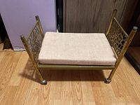 Mini metal bed frame with padded cushion on top, showing front and side floral design panels and legs with casters.