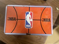 Close-up image of the rectangular metal tin box lid showing detailed basketball court texture and NBA logo in the center.
