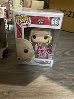 Front view of the WWE Trish Stratus Pop! vinyl figure in clear protective casing, showing signature in pink marker.