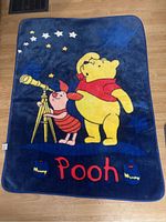 Front full view of the blue Winnie the Pooh blanket showing Pooh and Piglet with telescope and stars.