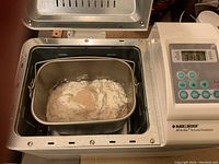 Photo showing interior of breadmaker with baking pan containing bread ingredients like flour and yeast for bread making.