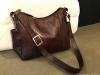 Brown leather LaDiva shoulder bag resting on a surface, showing overall shape and brass buckle on strap.