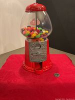Front view of red bubble gum machine filled with colorful jelly beans, quarter placed nearby for scale.