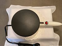 Top view of the electric crepe maker showing the round black cooking surface and white handle with power switch.