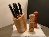 Wood knife block holding five knives with black handles, plus wood salt shaker and wood pepper grinder placed on white doily.