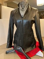 Front view of the black leather blazer-style jacket hanging on a Danier hanger, showing zipper and pockets.
