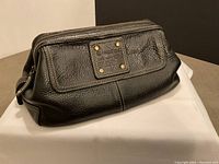 Front and partial side view of black leather Fossil toiletry bag on a surface showing structured shape and exterior details.