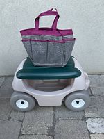 Front view of the gray and green rolling garden seat with the purple-trimmed gray mesh gardening bag placed on top, showing the garden seat's compact design and bag's exterior pockets.