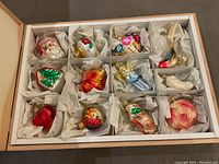Top view of the full 12-piece Inge-Glas ornament set in a large wooden box with compartments and protective paper wrapping each ornament.