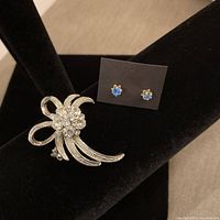 Image showing silver-toned rhinestone brooch and sapphire blue stone stud earrings on black display stand.