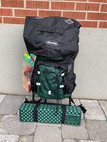 Front view of the hiking backpack showing black top compartment, green fabric with bungee cords, attached sleeping mat, and unopened Bota Bag packaging.