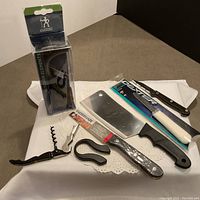 Overall view of all tools including sharpener, cleaver, corkscrew, ceramic knife, and clam shelling tool arranged on white cloth.