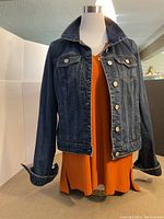 Front view of dark blue jean jacket worn open over orange Joseph Ribkoff sleeveless top on mannequin