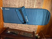 Blue Light Speed self-inflating air mat shown fully unrolled on carpeted floor with matching carry bag laying on top.