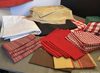 Overview of assorted folded table linens including napkins, placemats, and table cloths showing various fabrics and colors.