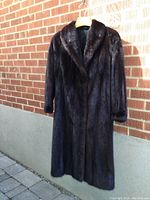 Front view of full-length dark brown mink coat hanging against brick wall