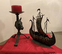 Both metal decorative pieces displayed on red cloth, horse head candle holder with red candle on left, Viking ship on right.