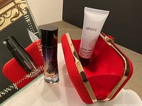 Photo showing Giorgio Armani perfume bottle, lotion tube, and bright red gold-accented evening bag with open clasp revealing red fabric interior.