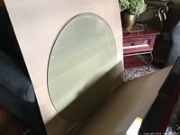 Full view of the round glass tabletop leaning against a cardboard backing showing the bevelled edge and general condition.