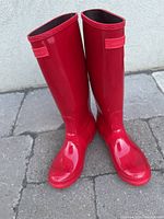 Pair of glossy red knee-high rain boots standing upright, showing front view.