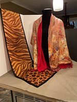 Long silk scarf with tiger-stripe and leopard print pattern and black border, shown flat and partially draped. Accompanied by reversible scarf draped on mannequin.