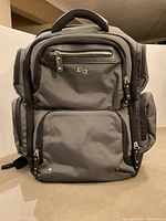 Front view of the SOLO backpack showing multiple zippered compartments and SOLO logo on front pocket.