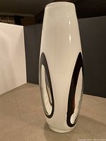 View of tall glass floor vase showing black and clear ovals on white background from one angle.
