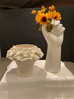 Photo showing both ceramic items side by side: the hand vase holding yellow artificial flowers and the flower pot with detailed rose relief.