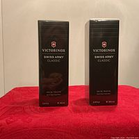 Front view showing both unopened black Victorinox Swiss Army Classic Eau de Toilette boxes standing upright on a red surface.