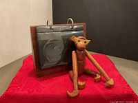 Wooden monkey figurine seated next to the wooden photo holder on a red surface, showing the overall condition and scale of the items.