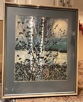 Full view of framed watercolour painting showing birch trees by water with silver frame and blue mat.